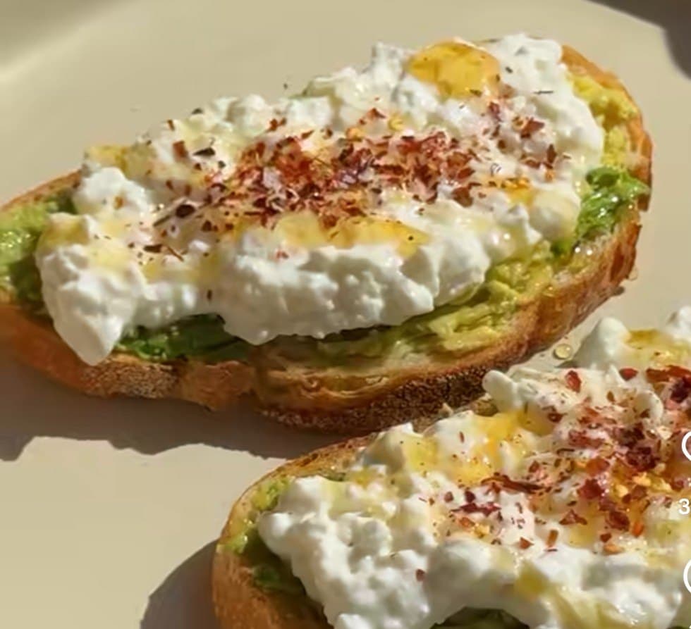 Two slices of sourdough with smashed avocado, cottage cheese, honey and chilli flakes
