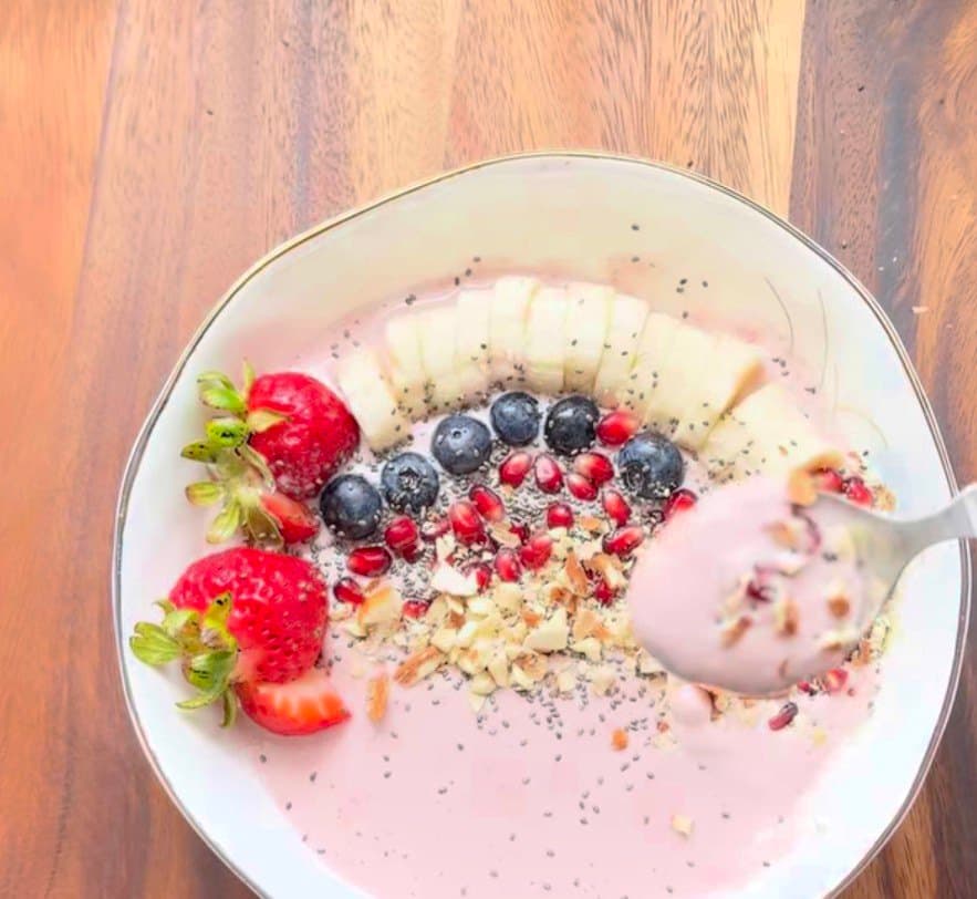 A bowl of pink yogurt oats topped with strawberries, blueberries, pomegranate seeds, chia seeds and almonds